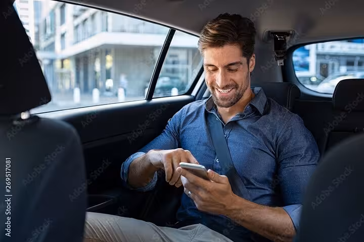 Smiling businessman using smartphone in backseat of private transfer car