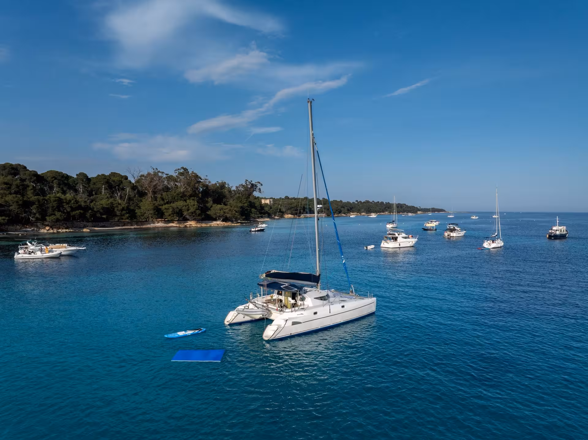White catamaran anchored in turquoise bay near Cannes with boats and lush island in background