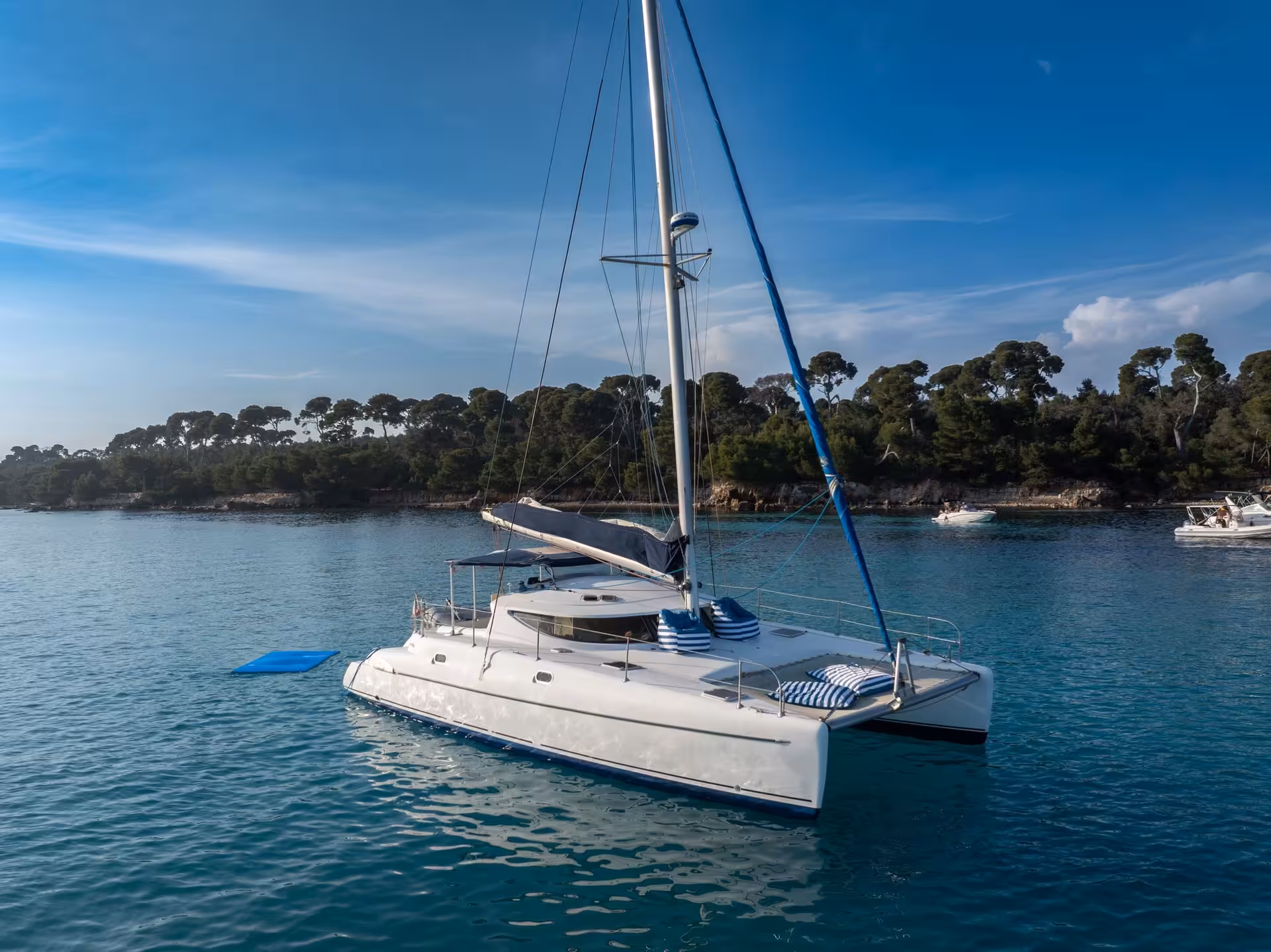 White catamaran anchored in turquoise waters near Cannes with blue striped cushions and forested island backdrop