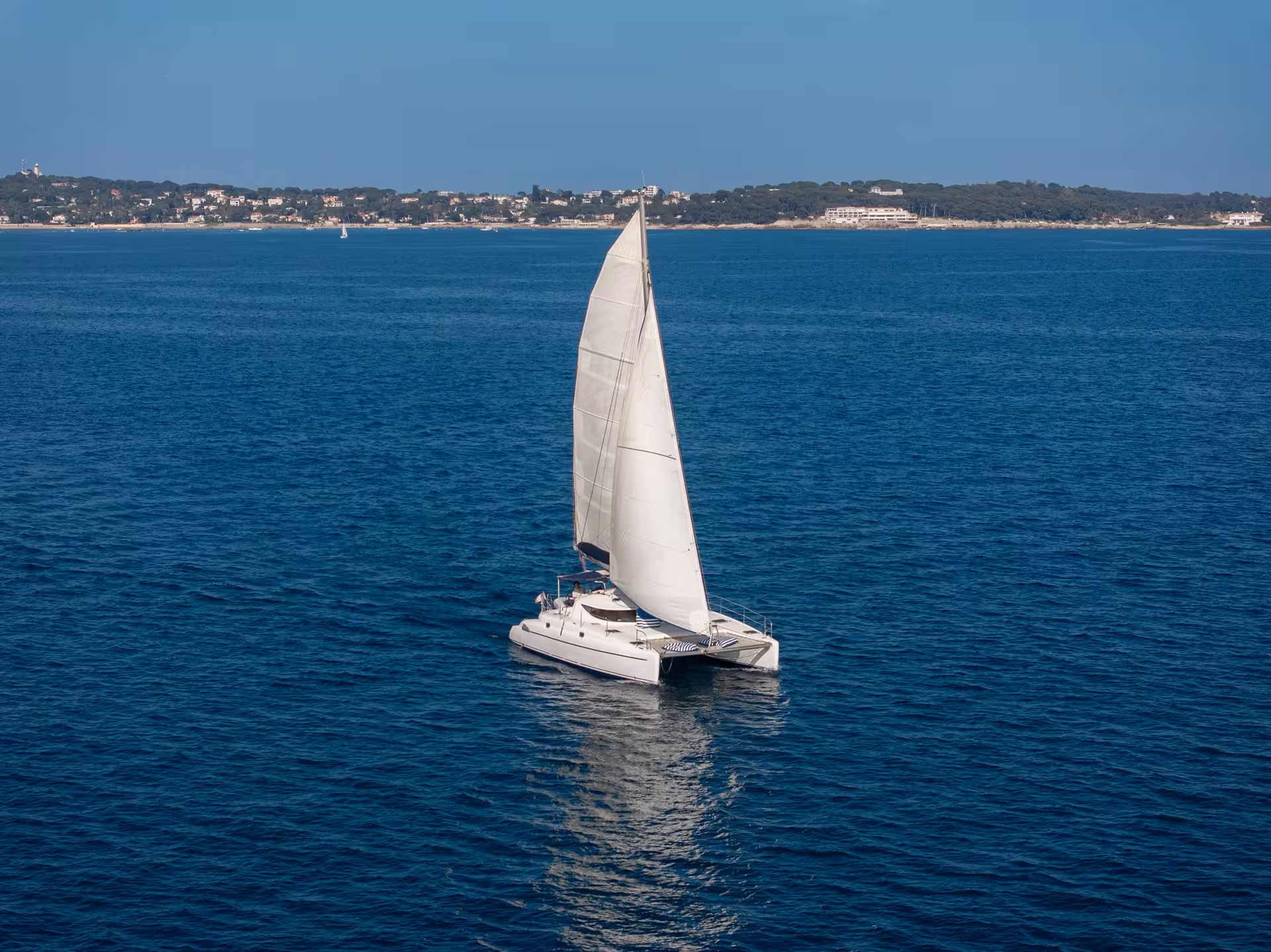 White catamaran sailing on blue Mediterranean sea near Cannes coastline on a sunny day