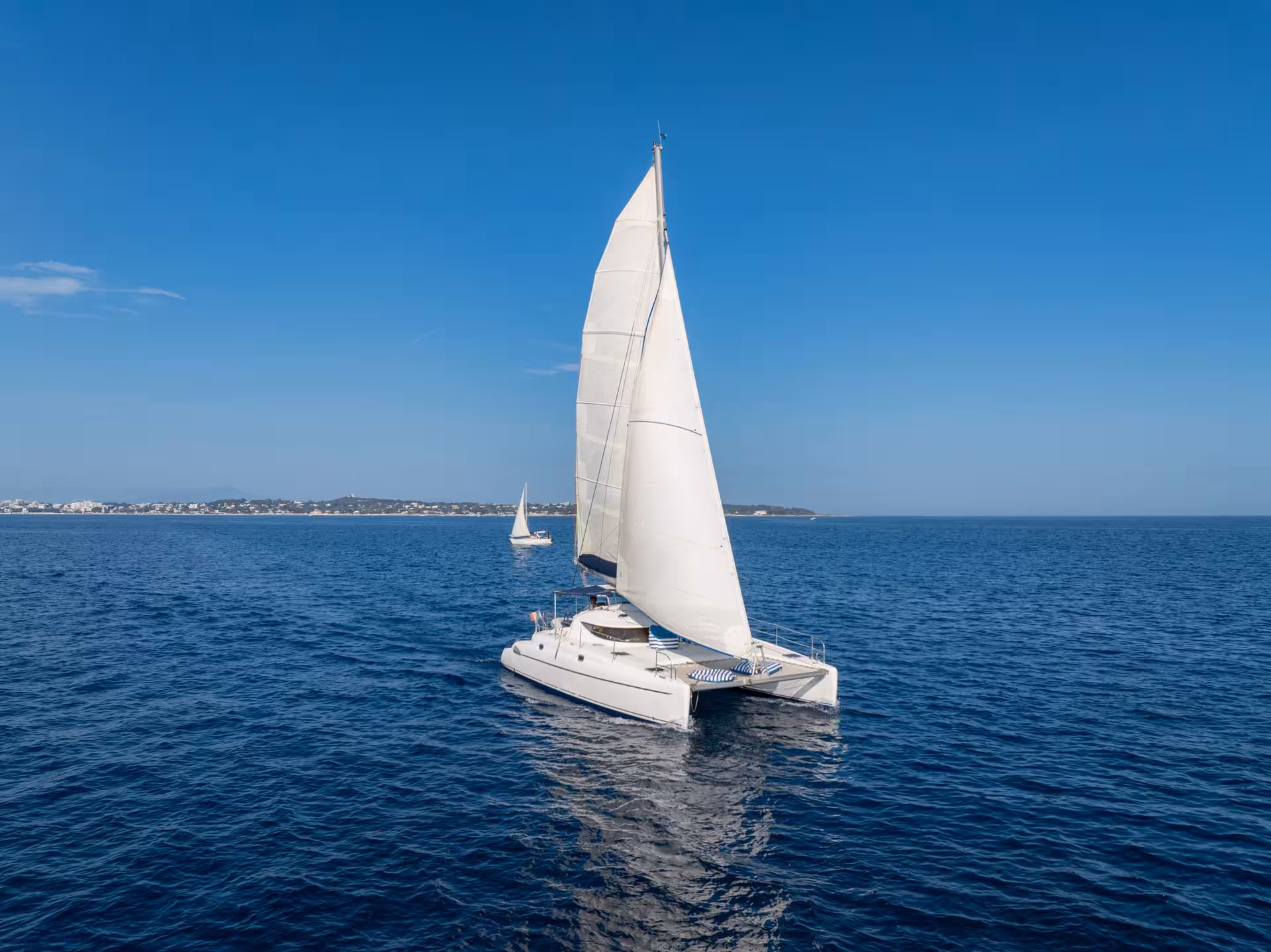 White sailing catamaran on calm blue sea near Cannes coastline on a sunny day