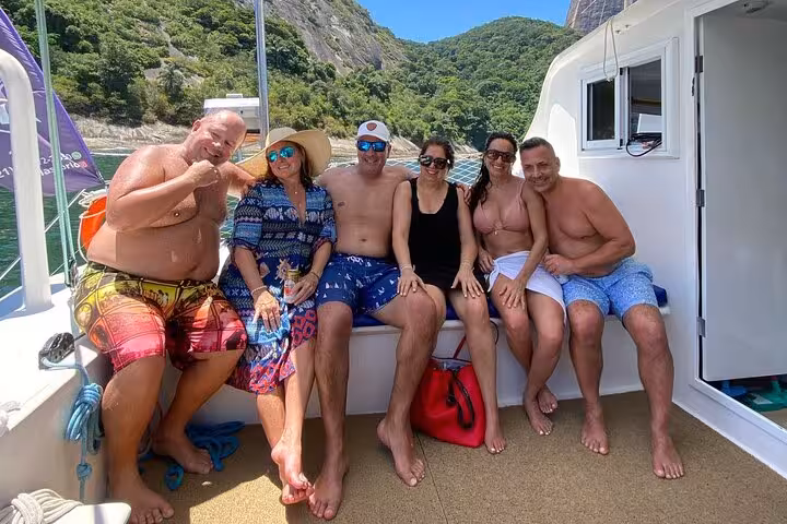 Group relaxing on Velas do Rio private catamaran with open bar, sailing Rio coastline and green hills