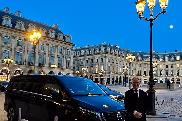 Private chauffeur in suit standing beside black Mercedes van at Place Vendôme Paris at dusk
