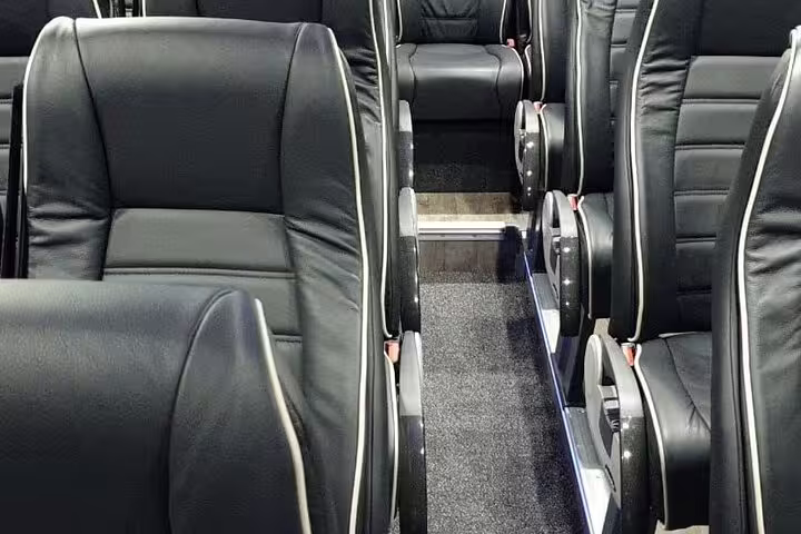 Luxury black leather seats inside a private chauffeur transfer coach with white piping trim
