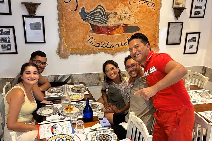 Smiling group enjoying their freshly cooked pasta meal in a cozy Roman trattoria setting.