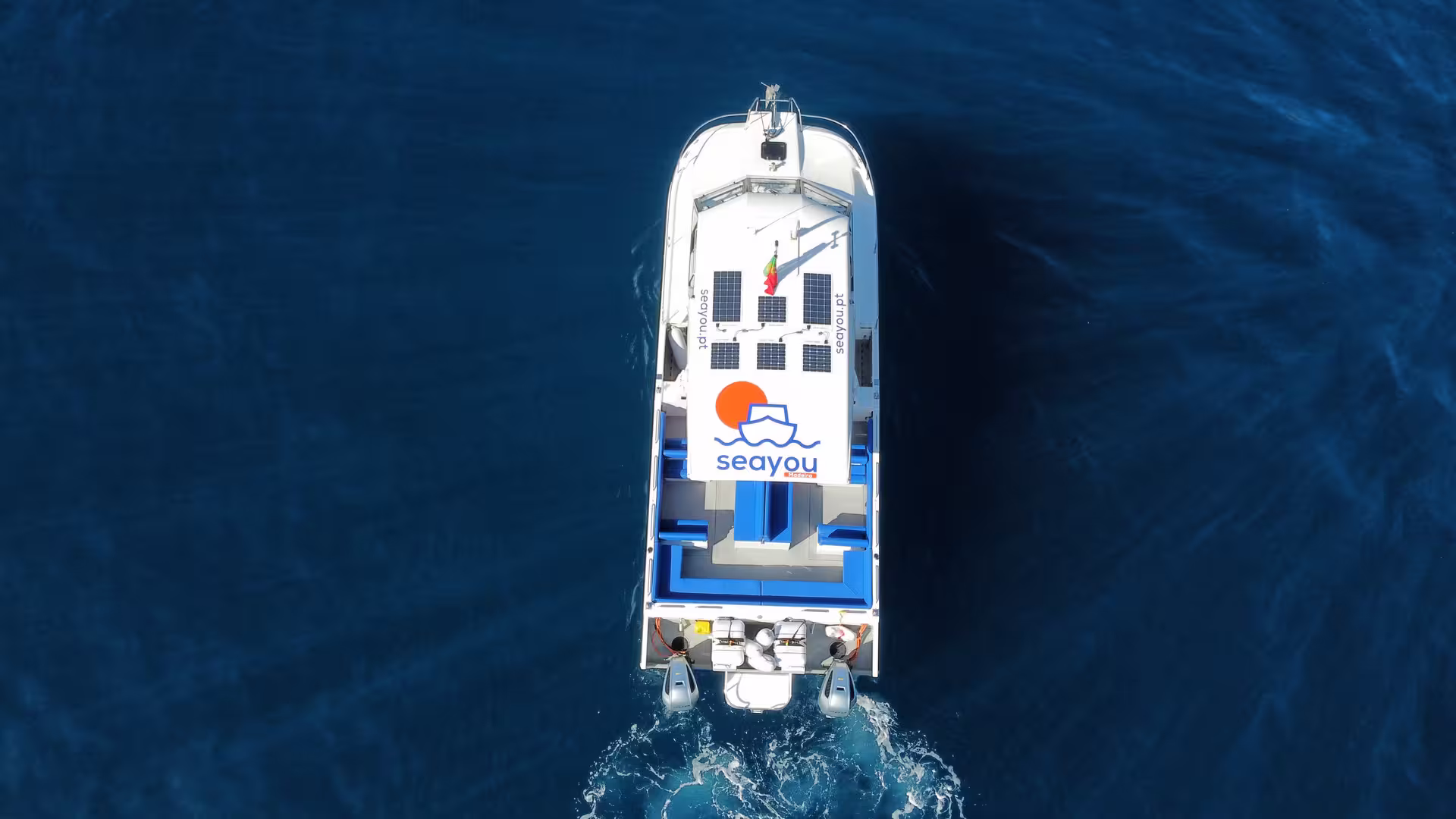 Aerial view of a private cruise boat with solar panels navigating the deep blue ocean for a sunset tour experience.