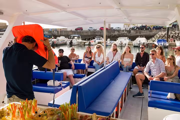 Guests seated on a private cruise boat, enjoying refreshments as a crew member demonstrates safety procedures.