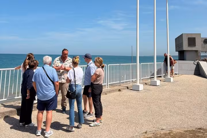 Tour guide speaking with a small group of visitors at Normandy D-Day beach overlook on a sunny day
