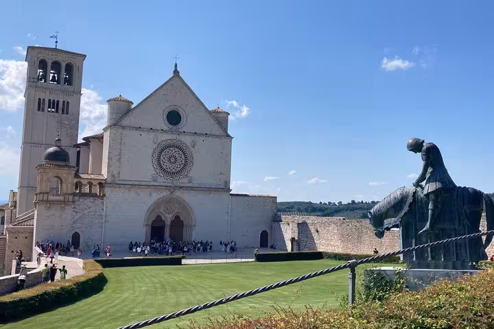 Private tour vehicle parked near the Basilica of Saint Francis in Assisi, showcasing iconic architecture under a clear blue sky.