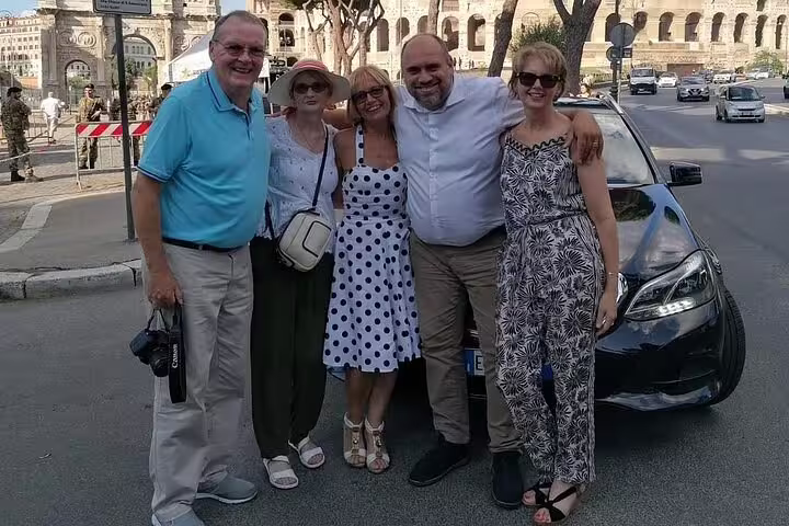 Happy group of tourists posing in front of a car near the Colosseum, enjoying their private day trip from Rome.