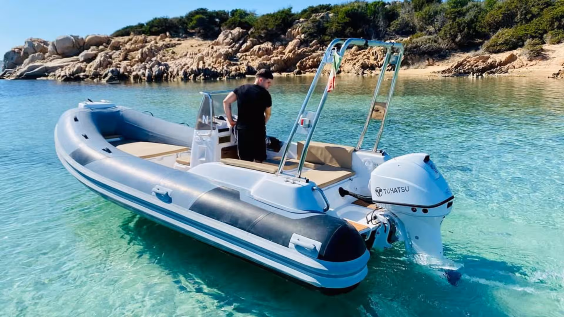 A private dinghy anchored in the transparent waters near a rocky shoreline in La Maddalena, Sardinia.