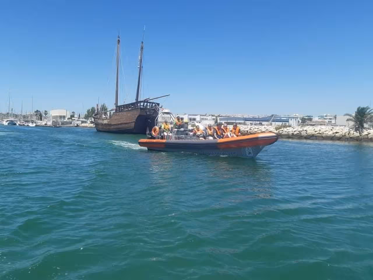 Guests in life jackets aboard an orange RIB speedboat departing Lagos marina for a private dolphin watching tour Algarve