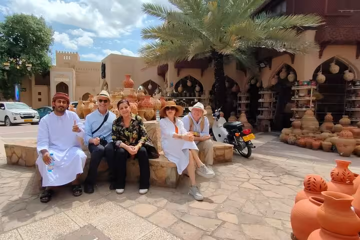 Happy small group with local guide relaxing by clay pots at Nizwa souq during a private evening cultural tour in Oman