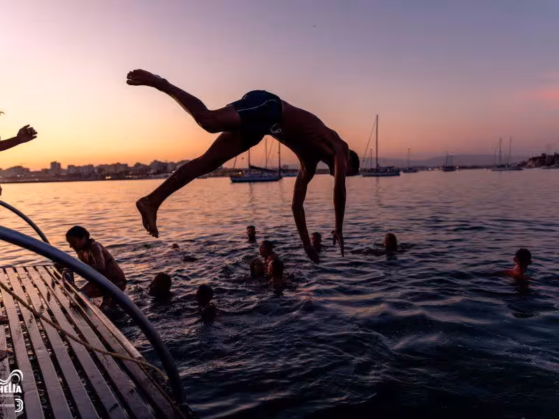 Group of friends enjoying a sunset swim and diving from a boat during a private event in a scenic bay.