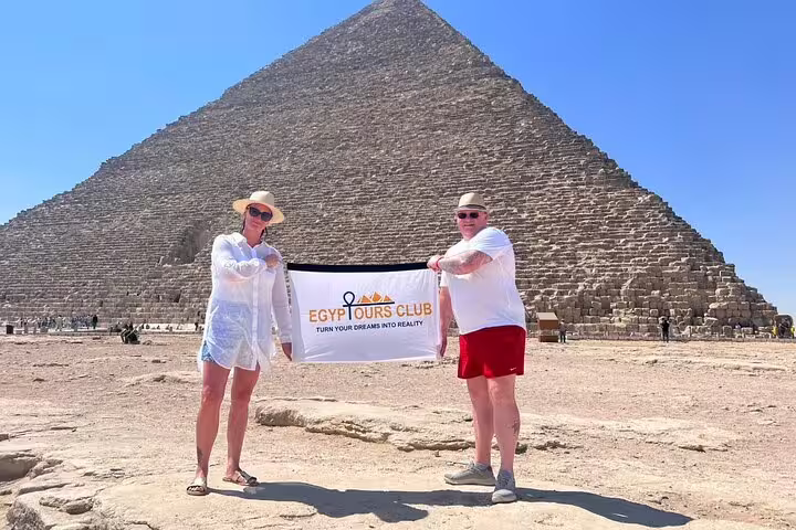 Tourists holding Egypt Tours Club banner at the Great Pyramid of Giza on a private Cairo day tour