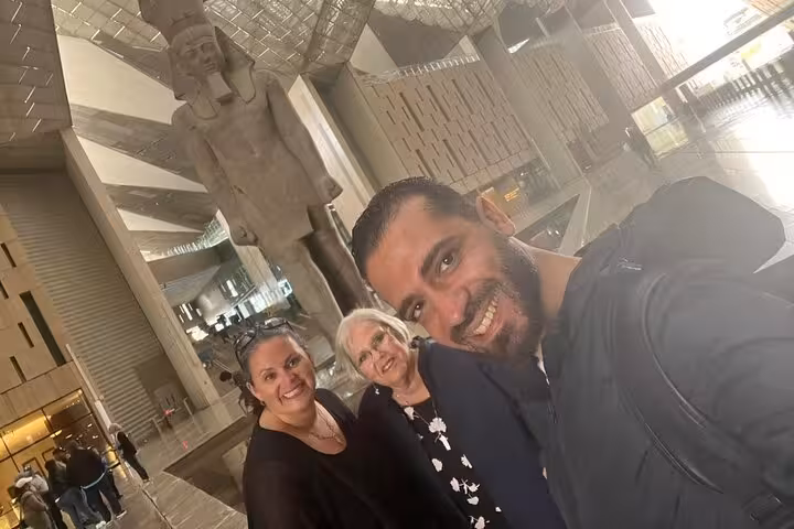 Guests with private guide at Grand Egyptian Museum atrium beside colossal pharaoh statue, Cairo tour