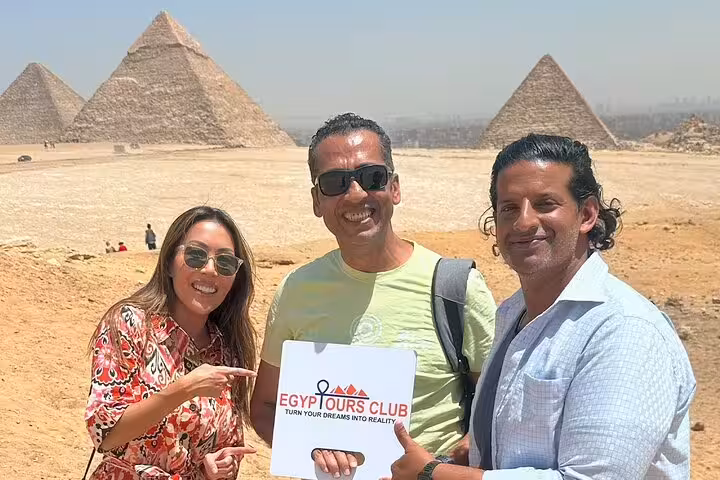 Private Giza Pyramids tour group with guide holding Egypt Tours Club sign, Cairo desert panorama backdrop