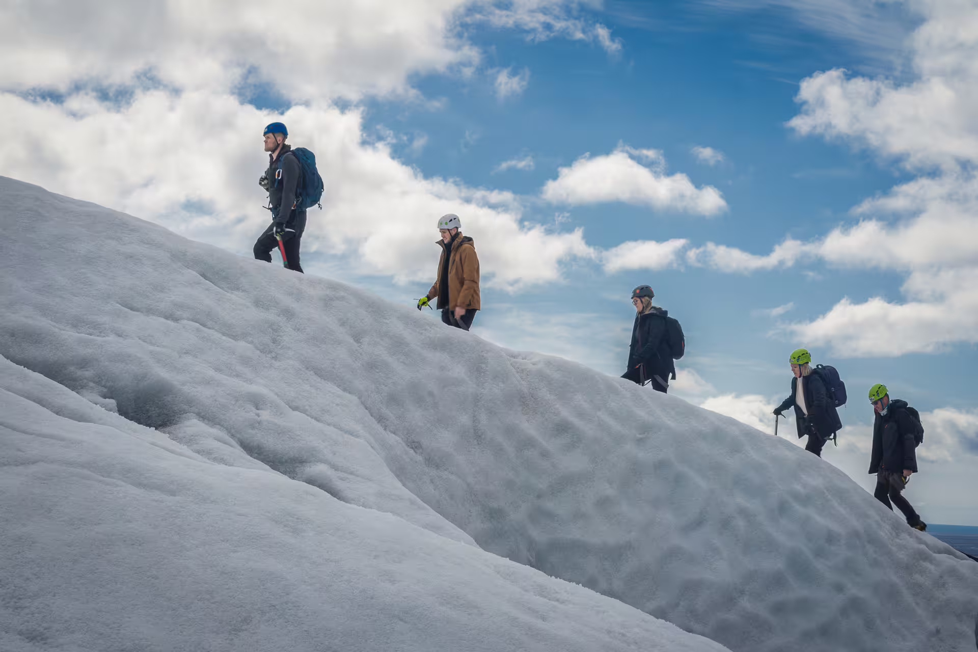 Group of four hikers with helmets trekking across a snow-covered glacier under a blue sky in Skaftafell