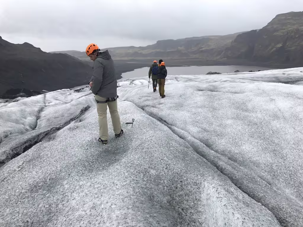 Hikers with orange helmets and crampons walking on a glacier with a lake and mountains in the background
