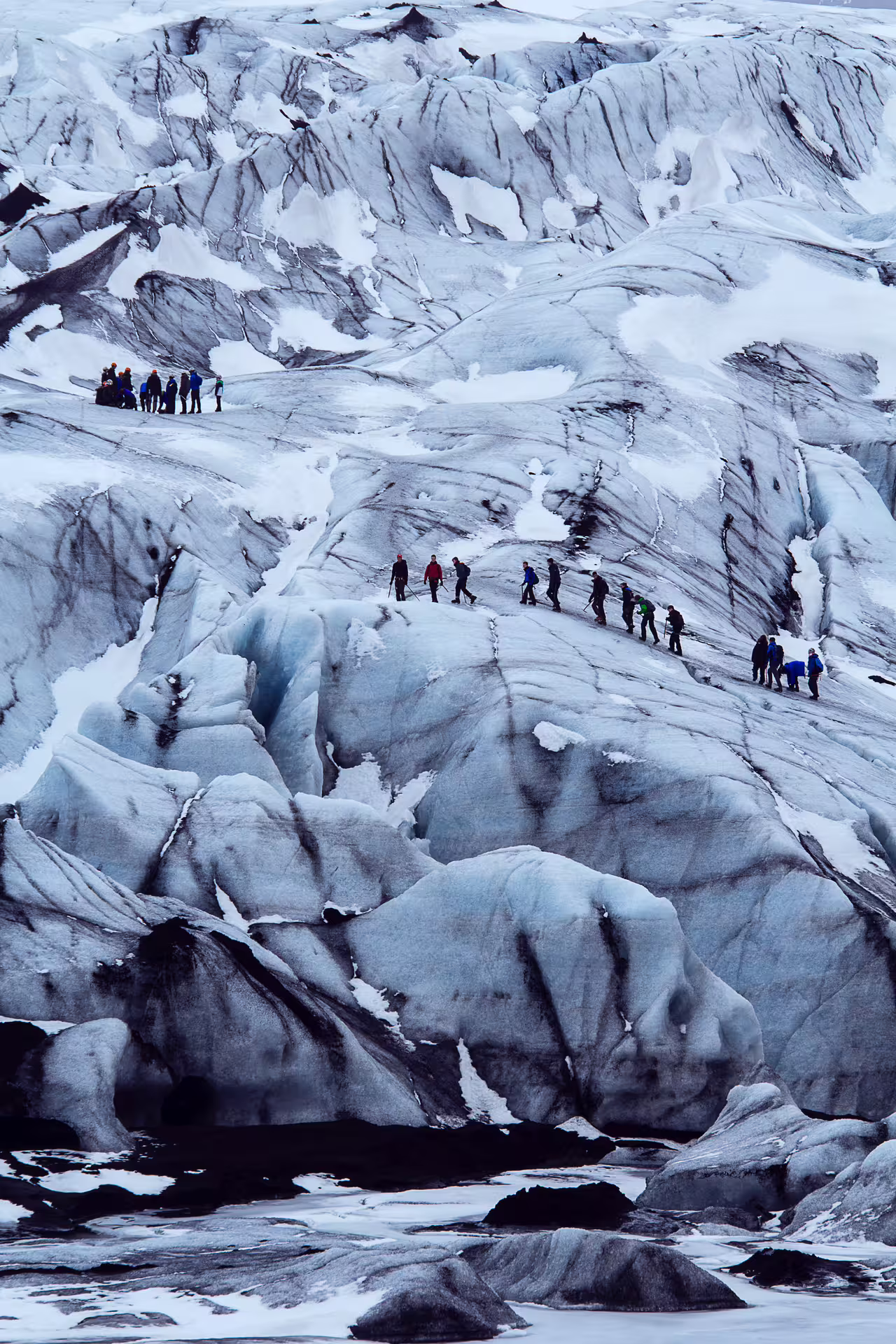 Group of hikers trekking across a vast glacier with crevasses and blue ice formations