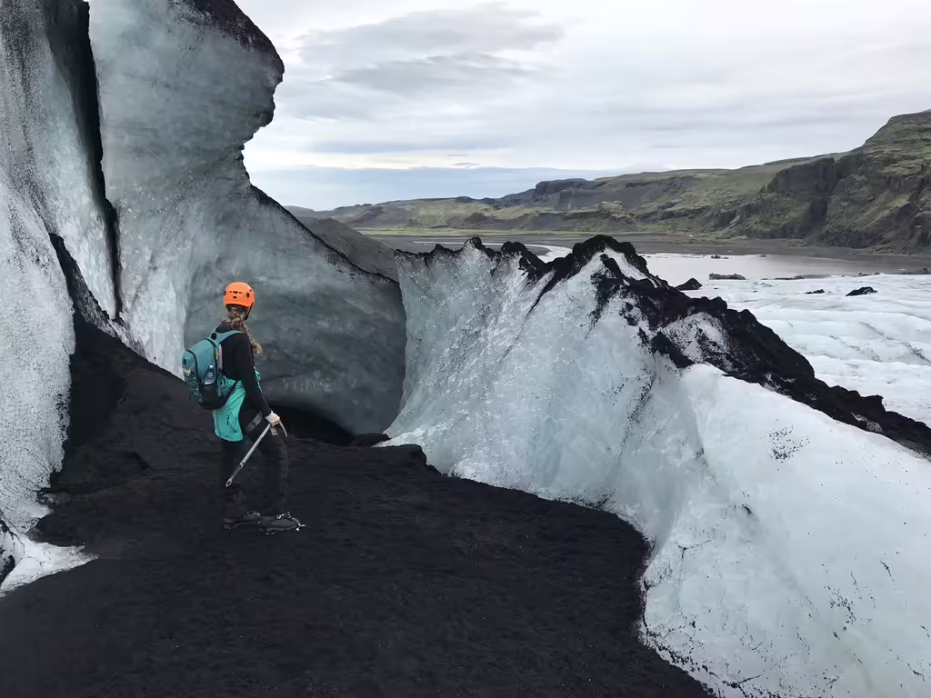Guide in orange helmet exploring black volcanic ash and ice formations on a South Coast glacier hike