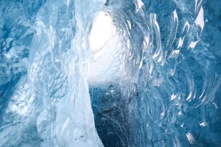 Lone traveler touches glowing blue glacier ice cave walls beneath an arched opening on a private tour