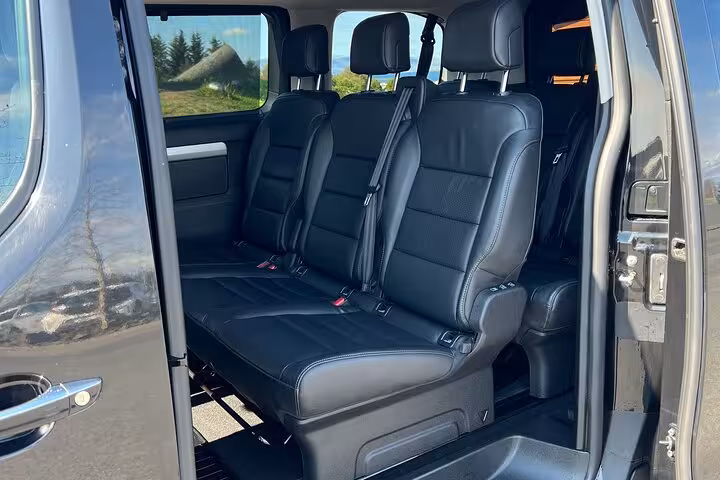 Black leather three-seat bench inside private tour vehicle with sliding door open