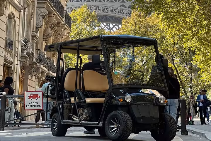 Black golf cart parked near the Eiffel Tower on a Paris street with Haussmann architecture