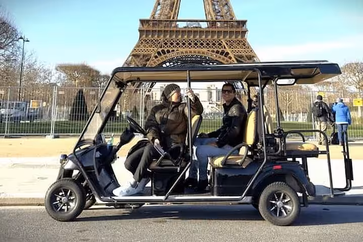 Two tourists riding a black golf cart tour vehicle in front of the Eiffel Tower in Paris