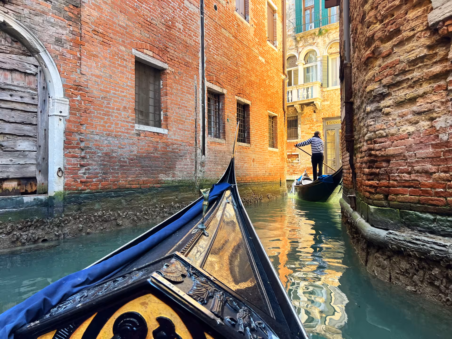 Experience romance on a private gondola navigating a narrow Venetian canal lined with historic brick buildings.