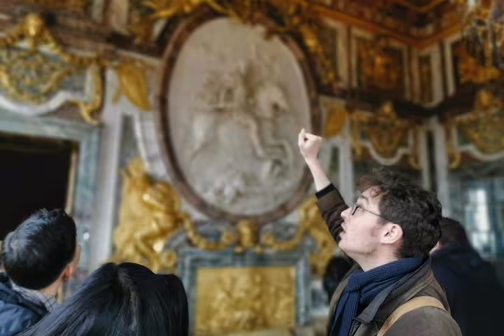 Private guide explains gilded Versailles Palace room to visitors during a private day tour from Paris