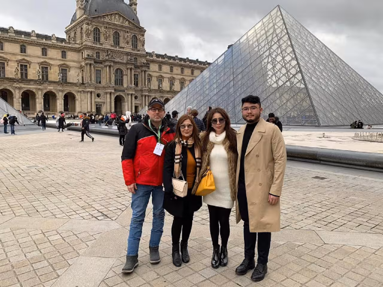 Group of four tourists posing in front of the Louvre Pyramid in Paris on a private guided tour