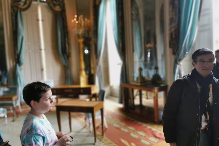 Guests on a private guided Versailles Palace tour from Paris, exploring ornate rooms with tall windows and drapes