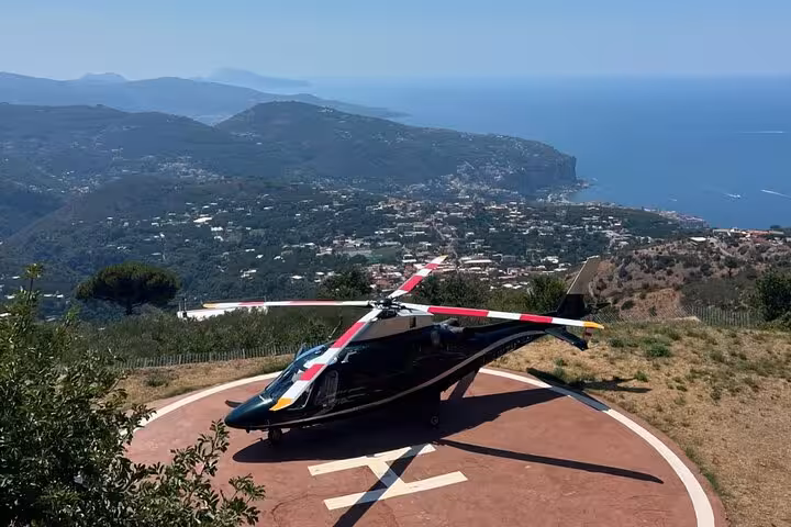 Black private helicopter on hilltop helipad overlooking Mediterranean coastline and lush green mountains