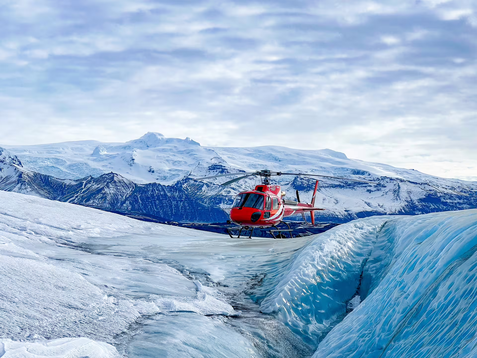Red helicopter landed on Vatnajökull glacier with snow-capped mountains in background, Skaftafell Iceland