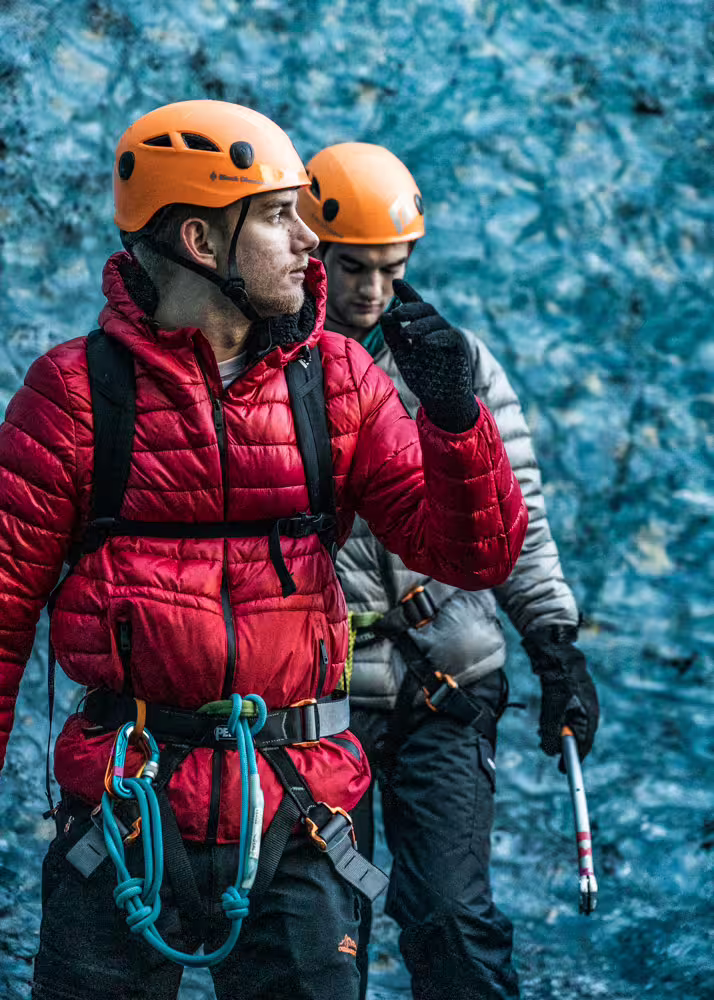 Two climbers with harnesses and ice axes standing before vivid blue glacier ice wall on a private climbing tour