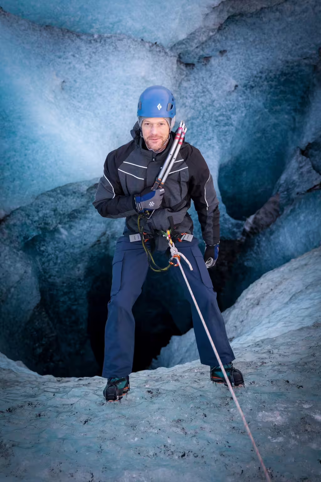 Adventurer in blue helmet and harness poses with ice axes inside a stunning private glacier ice cave tour