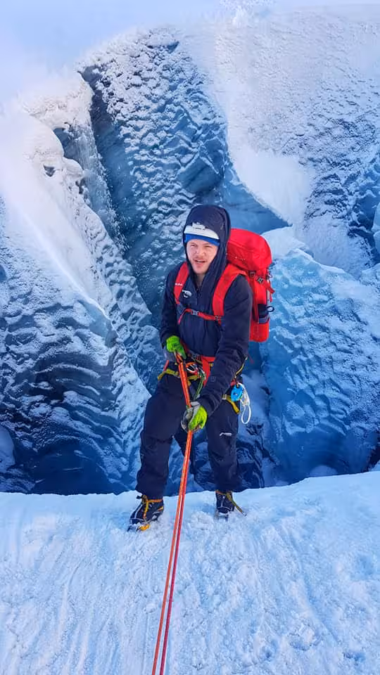 Ice climber with red backpack and rope on Solheimajokull glacier crevasse, Iceland