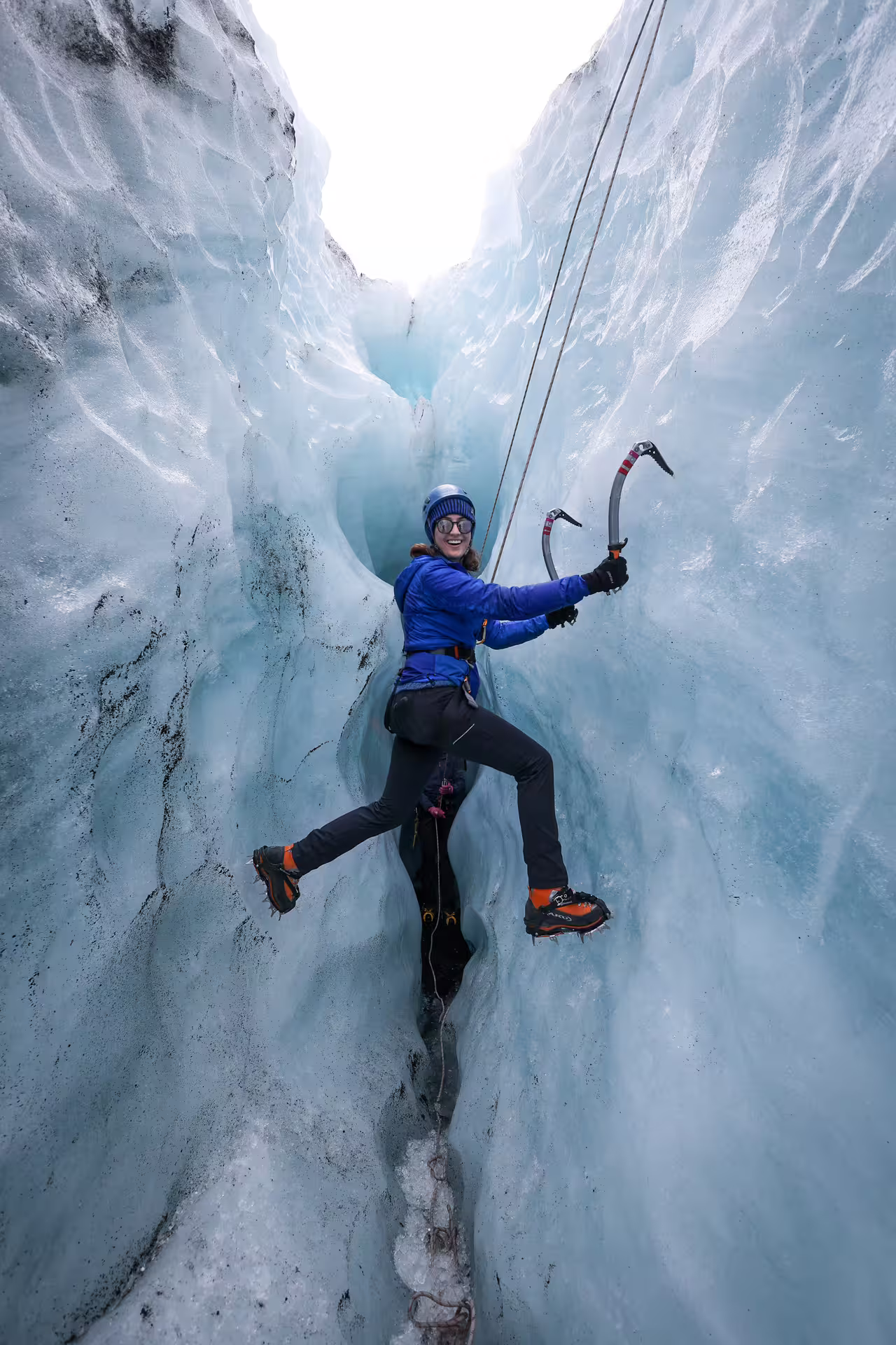 A climber wielding ice axes scales a narrow blue ice crevasse on Solheimajokull Glacier private tour.