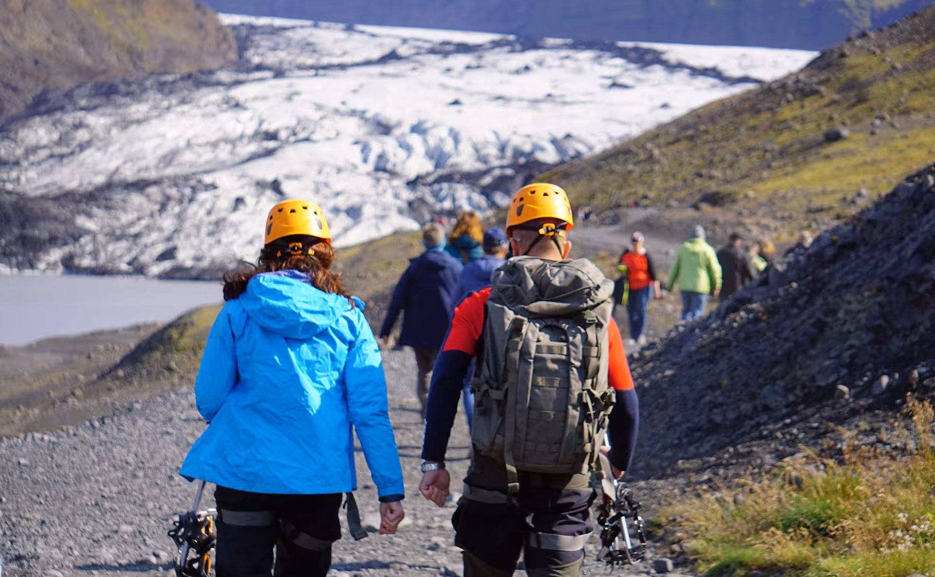 Group of hikers in yellow helmets walking toward Solheimajokull glacier on a rocky trail