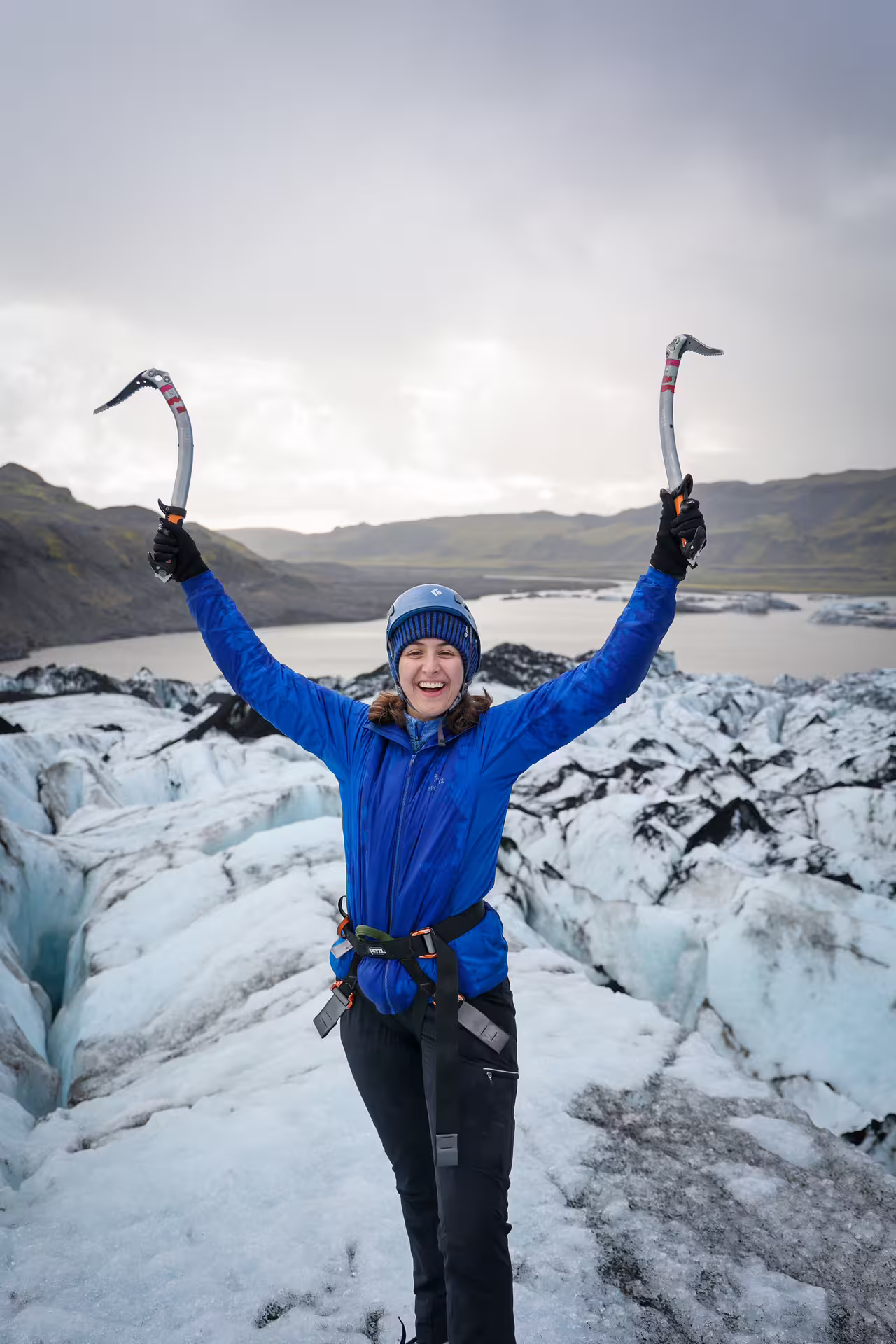 Excited climber raising ice axes triumphantly on Solheimajokull Glacier during a private ice climbing tour in Iceland
