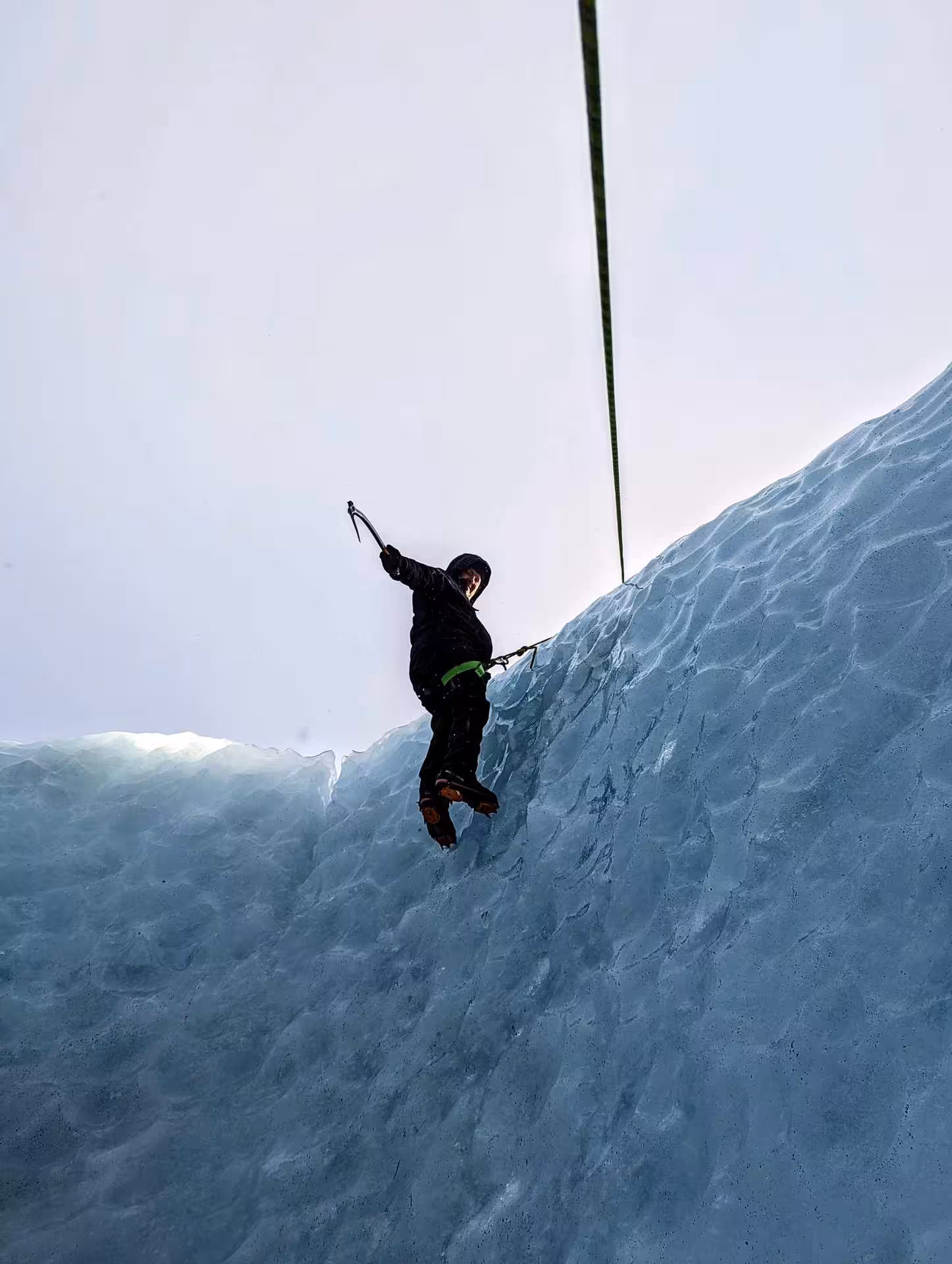 Ice climber scaling steep glacier wall with ice axe and crampons on Solheimajokull