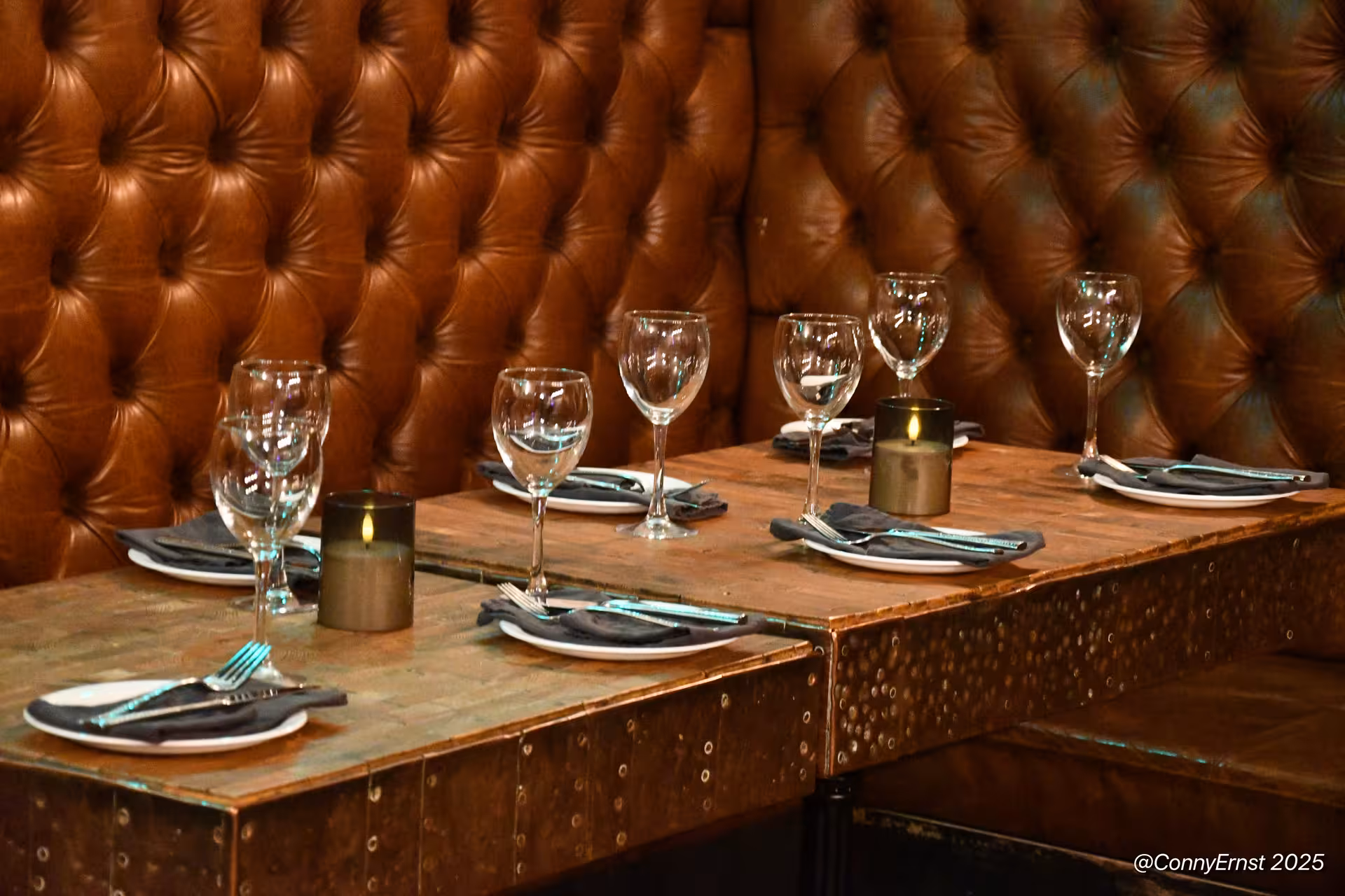 Elegant restaurant booth with tufted leather seating, set dining tables, wine glasses, and candlelight in Reykjavik