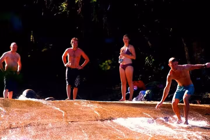 Tourists enjoy a natural waterslide during a private jeep tour in Paraty, surrounded by lush forest scenery.