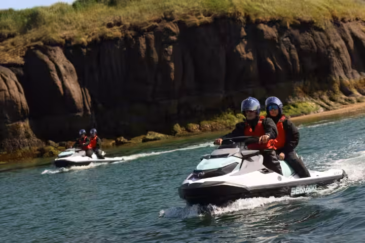 Two riders on a Sea-Doo jet ski near rocky cliffs during a private jet ski tour in Iceland