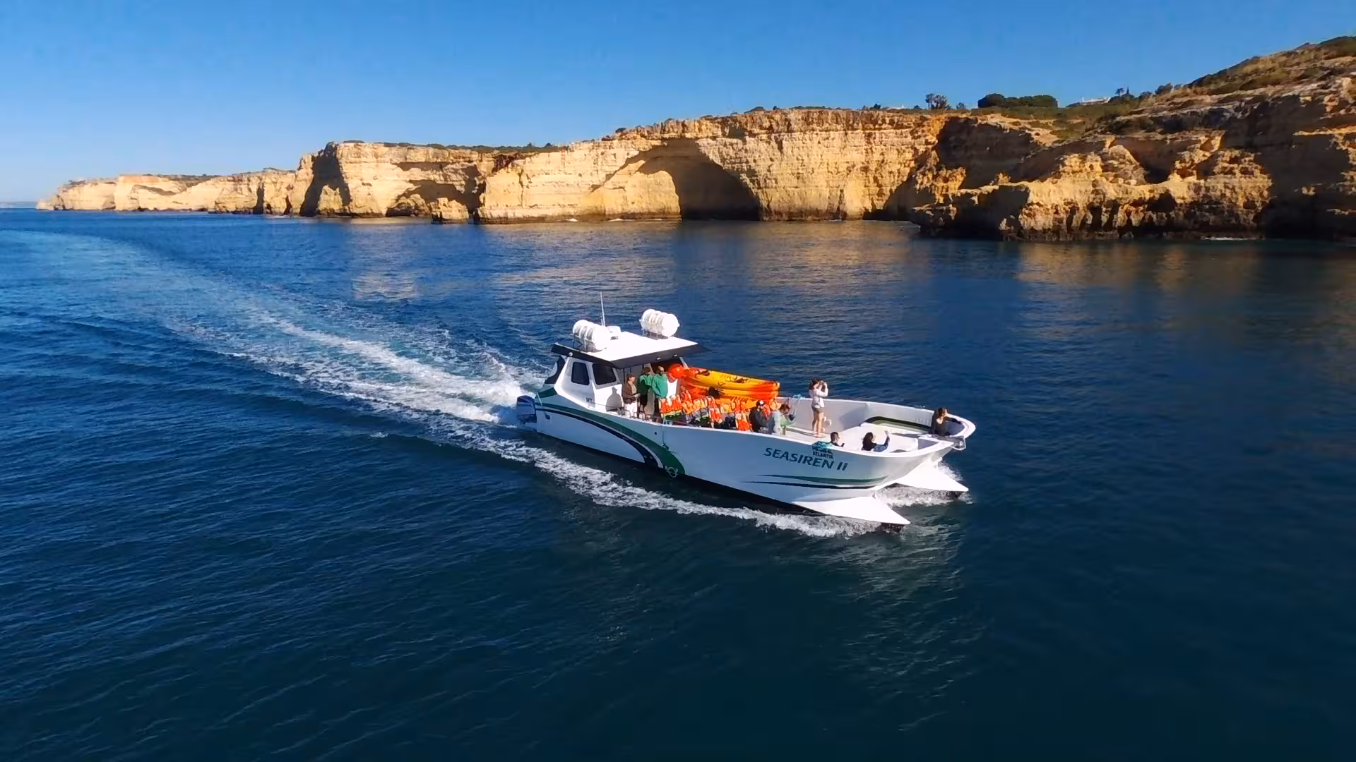 Seasiren II boat carrying kayaks and guests along the Algarve coast on a private kayak tour past golden limestone cliffs and arches