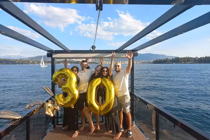 Celebratory group holding golden balloons on a private Lake Geneva cruise with stunning water views.