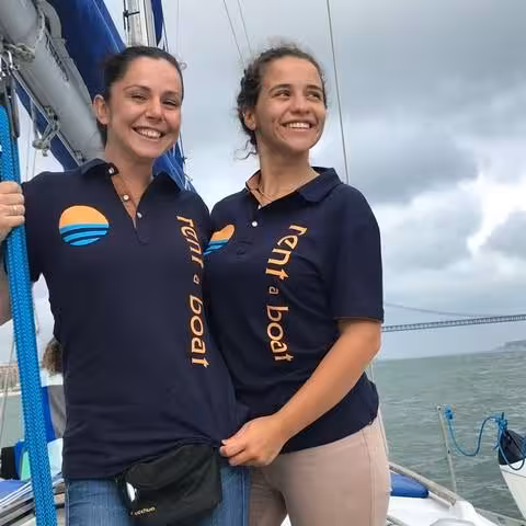 Crew on a private Lisbon sightseeing cruise sailboat near the 25 de Abril Bridge on the Tagus River in Portugal
