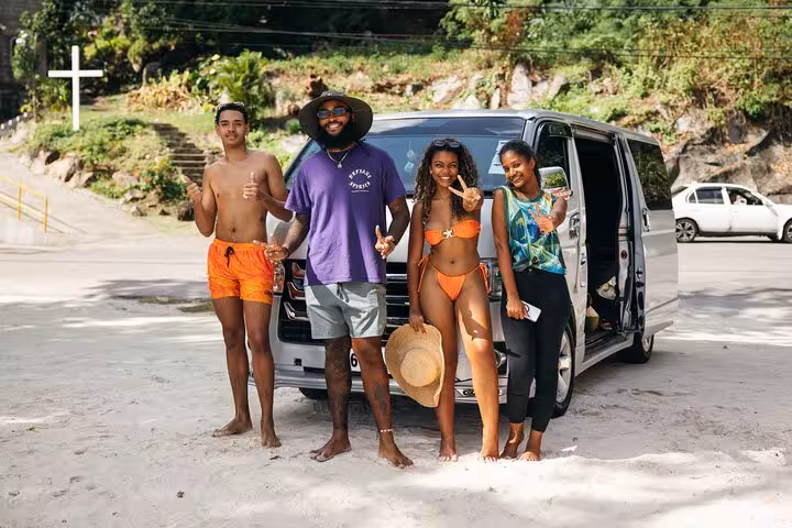 Group of tourists enjoying a private Mahe island tour, standing by a van on a scenic beach.