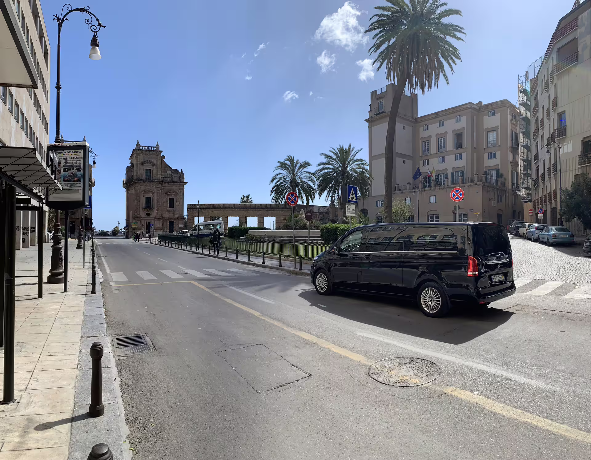 Black minivan for private Palermo Airport transfer driving past historic buildings and palm trees in Palermo city center